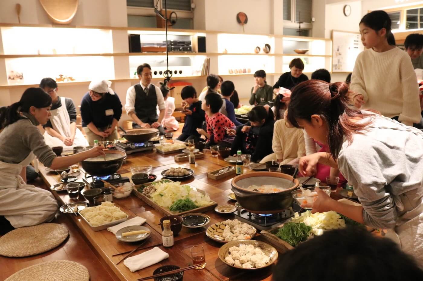 写真:囲炉裏を囲んで楽しそうに仲良く食事をする保護者や子どもたち。食事の配膳するスタッフたち