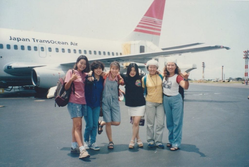 写真:友人たち(5人)と一緒に海外旅行へ旅立つ前にジャンボジェット機の前で記念撮影する忍足さん