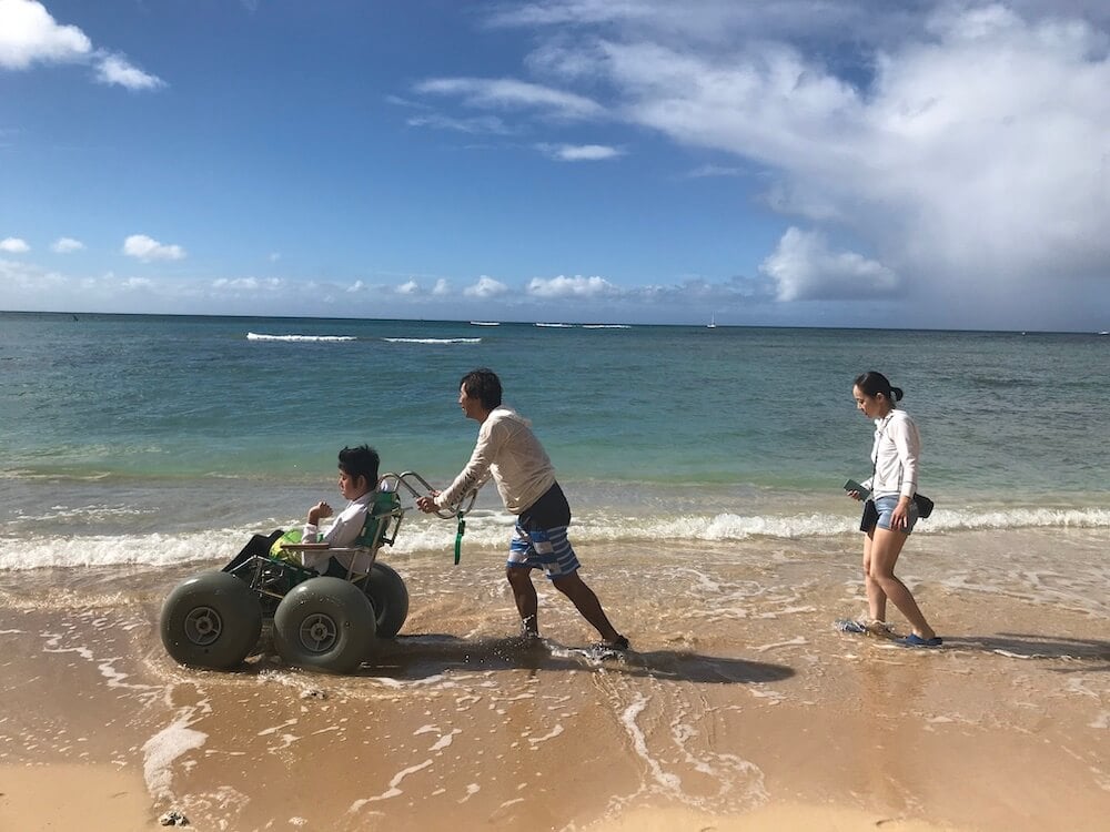 写真:海辺の散歩を楽しむ車いす利用者とその家族