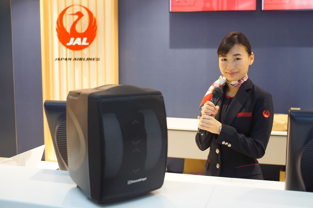 写真: ミライスピーカーと、そのマイクを手に持つキャビンアテンダントの女性