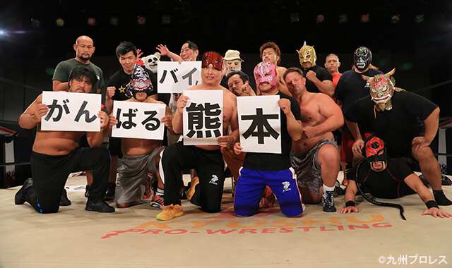 写真:リング上に集合し「がんばるバイ熊本」のプレートを胸に掲げる九州プロレスの選手たち