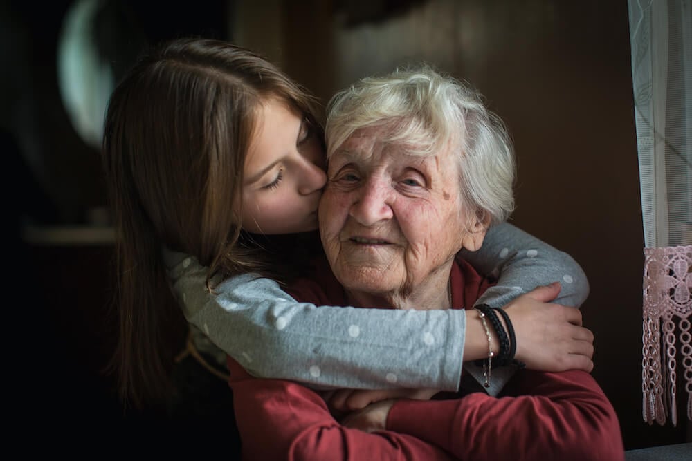 写真:祖母を後ろから抱きしめ頬にキスをする外国人の少女