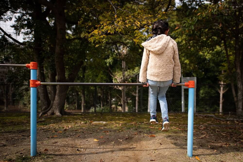 写真:公園の鉄棒の上に座り、背中を向けた少女