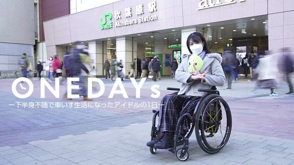 画像:駅の前で決めポーズをとり笑顔を向ける車いすに乗った猪狩ともかさん