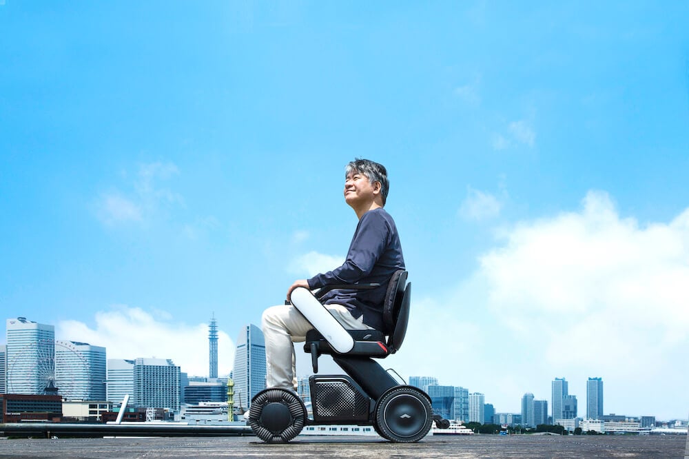 写真:横浜のビル群が背景に見えるハーバーサイドを「WHILL」で走行する中年男性