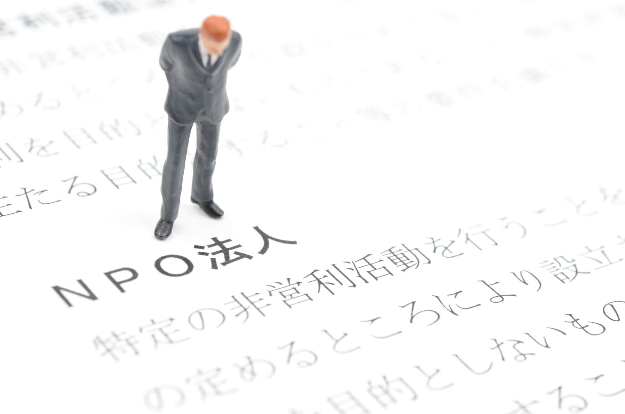 イメージ：NPO法人の説明をながめるスーツを着た男性のフィギュア