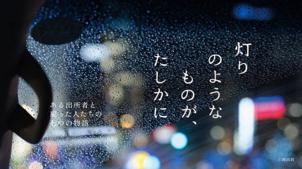 画像:職親プロジェクトドキュメンタリーシリーズの1シーン。画面中央に「灯りのようなものが、たしかに」の文字、画面左下に「ある出所者と雇った人たちの七つの物語」の文字、画像右下に「©岡田敦」の文字。