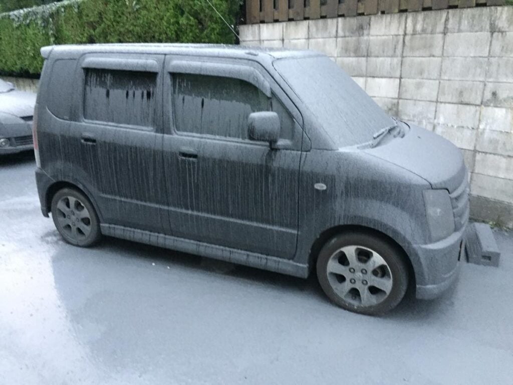 火山灰にすっぽりと覆われた軽自動車。黒の車体が完全に灰色に変色し、雨で灰が流れた跡が縦縞模様のように残っている