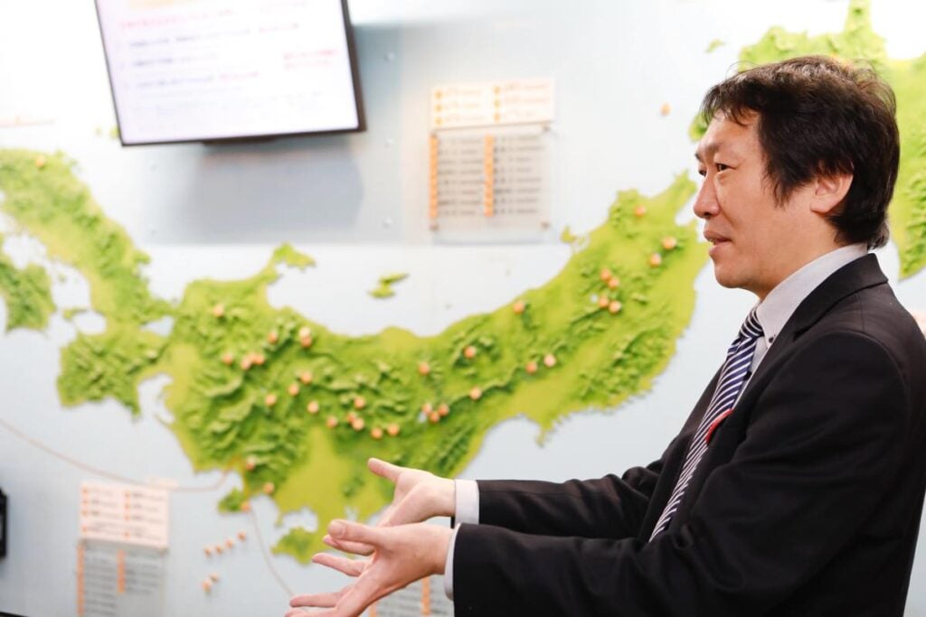 館内に展示された日本全国の火山の分布図の前で解説をする豊村さん