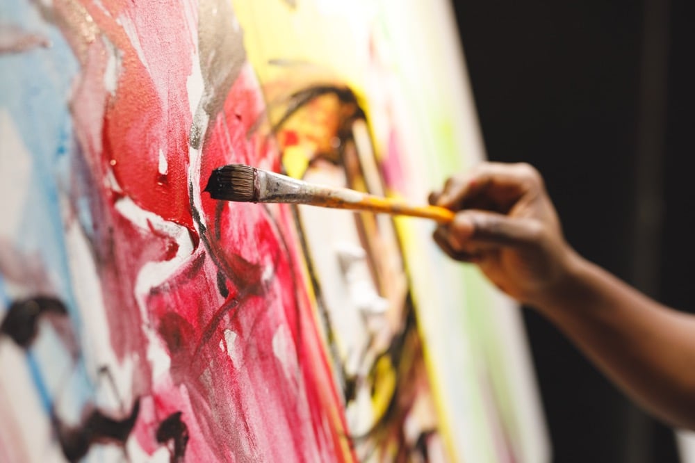 キャンバスに向かい、筆を使って鮮やかな赤や黄色の絵具で力強く絵を描く手元のアップ