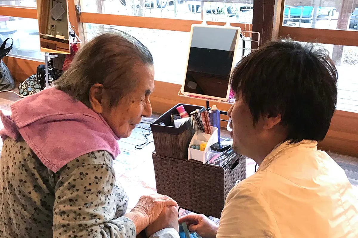 訪問理美容のサービスとして、理美容師が施設や自宅を訪問し、高齢の女性の髪をカットしている様子。