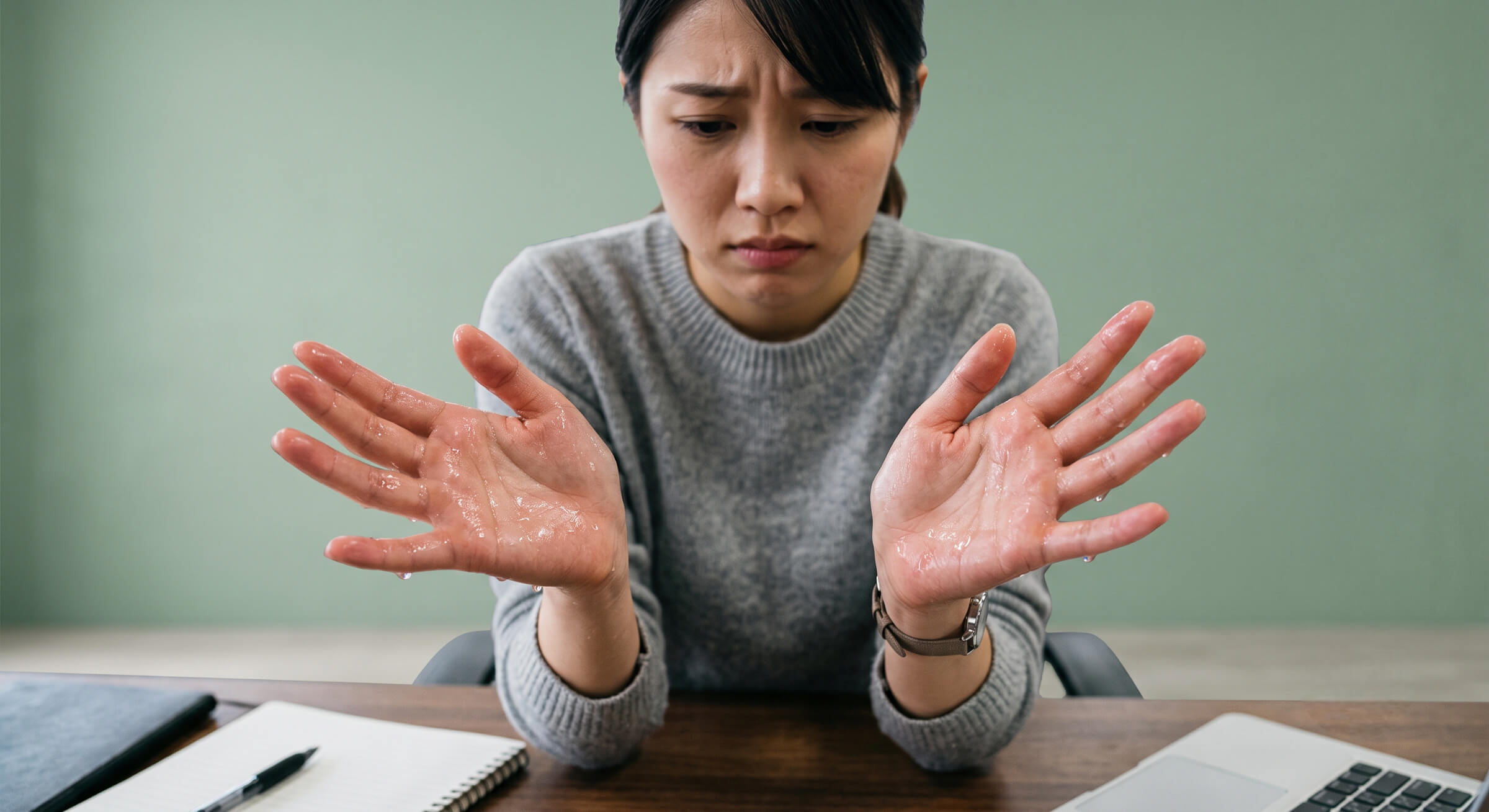 日常生活に支障が出るほどの手汗（原発性局所多汗症）に悩む女性。両手のひらから汗が滴り落ちており、不安げな表情で自分の手を見つめている。