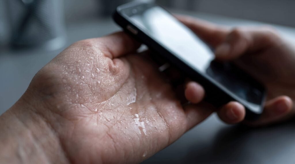 日常生活に支障が出るほどの手汗(原発性局所多汗症)に悩む人。スマートフォンを操作しているが、手のひらに大量の汗が滲んでいる。