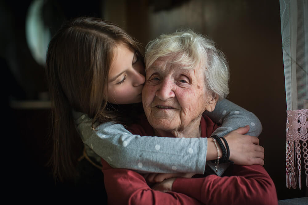 写真：祖母を後ろから抱きしめ頬にキスをする外国人の少女